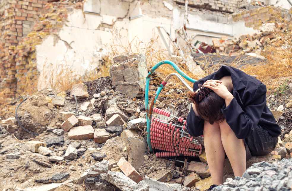 A girl next to a house destroyed by earthquake
