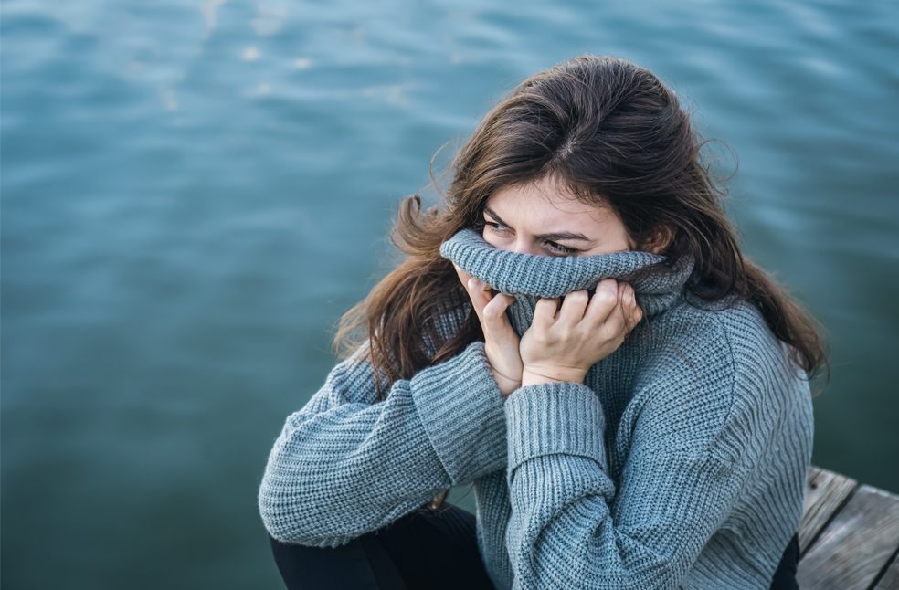 Woman sitting by river in winter