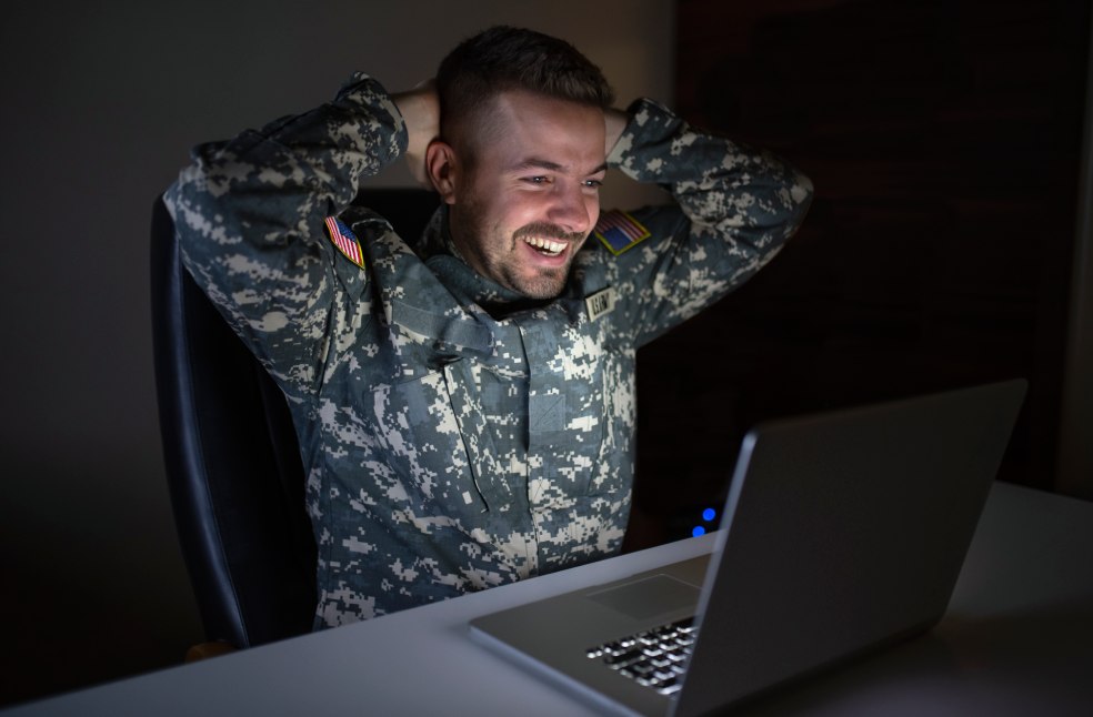 Caucasian soldier in army uniform in front of computer feeling happy and excited.