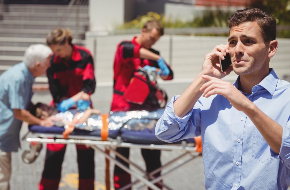 Man talking on mobile phone and paramedics examining injured boy