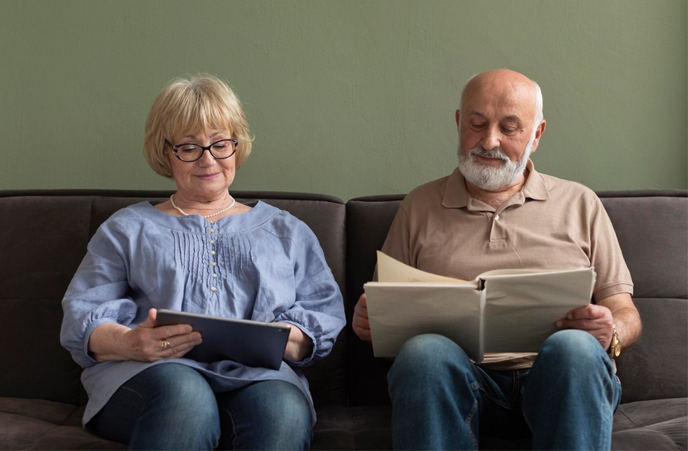 Old couple reading a newspaper and tablet respectively