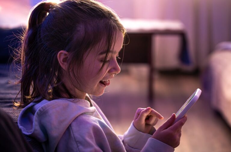 Australia enforces strict age checks for adult content access A little girl uses a smartphone while sitting in her room