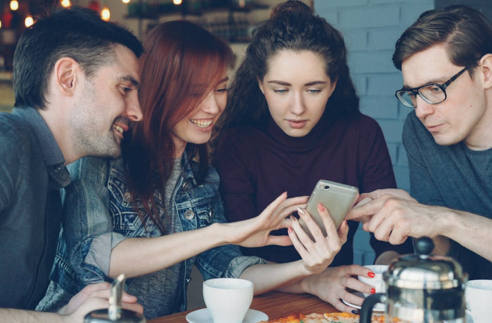 Friends enjoying coffee together while using phones, reflecting social media addiction