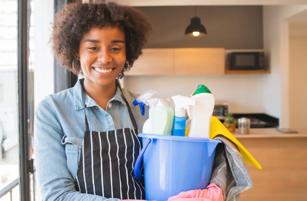 Afro woman holding a bucket with cleaning items
