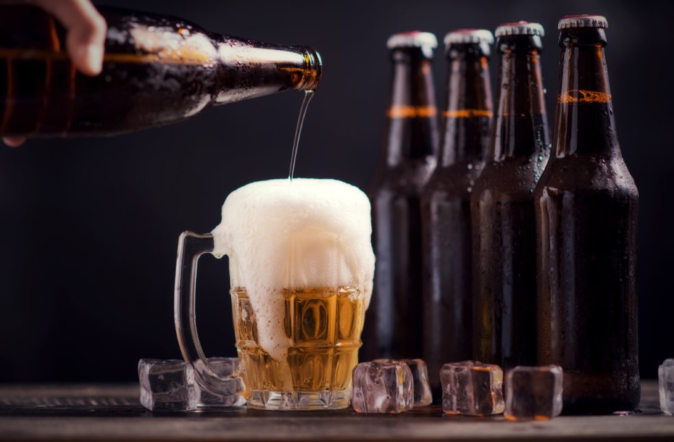 Glass bottles of beer with glass and ice on dark background