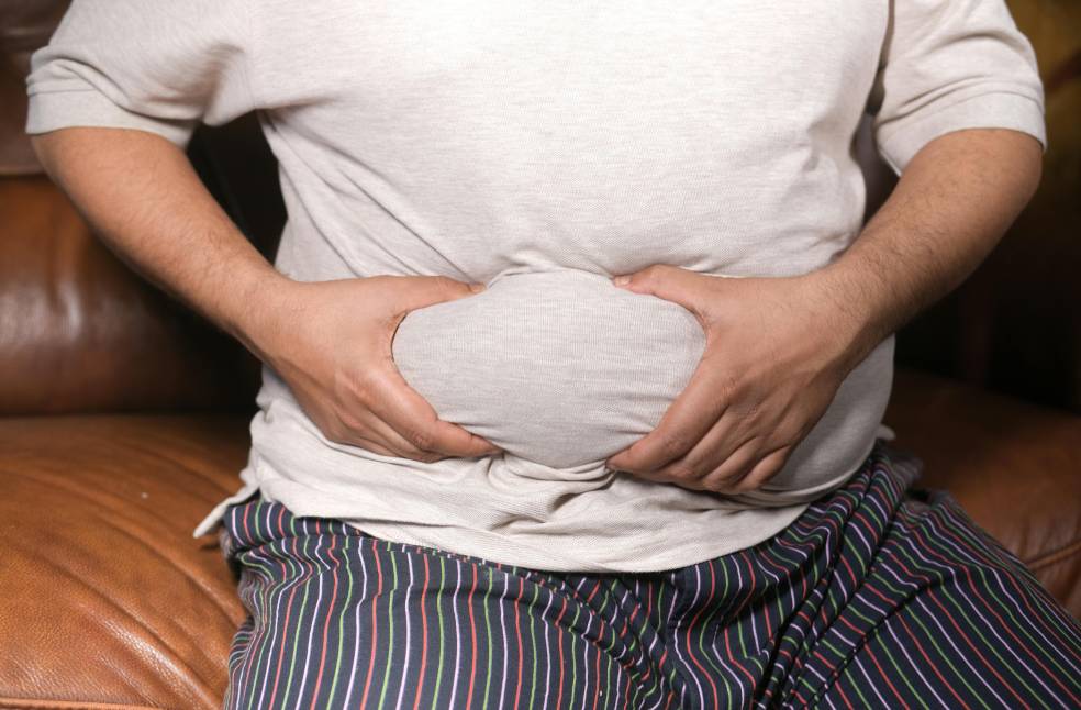 A close-up view of a man holding his tummy while sitting on a couch