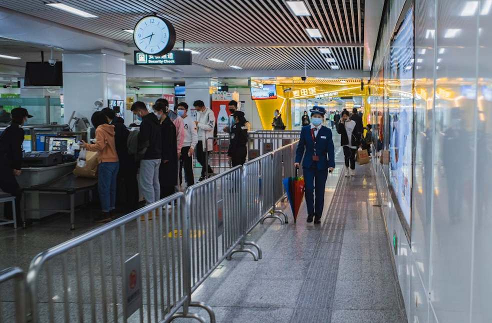 Travelers passing through airport security with staff and metal railings visible