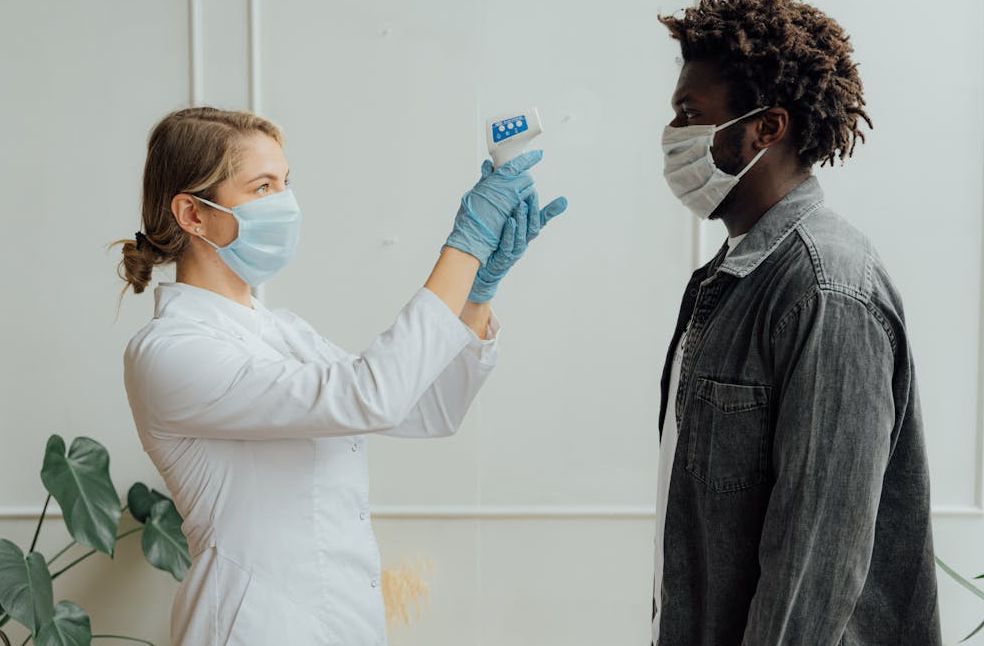 A healthcare worker measures a patient's temperature with a forehead thermometer