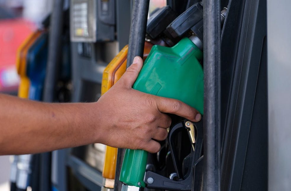Close-up of a hand holding a green fuel nozzle at a gas pump station outdoors