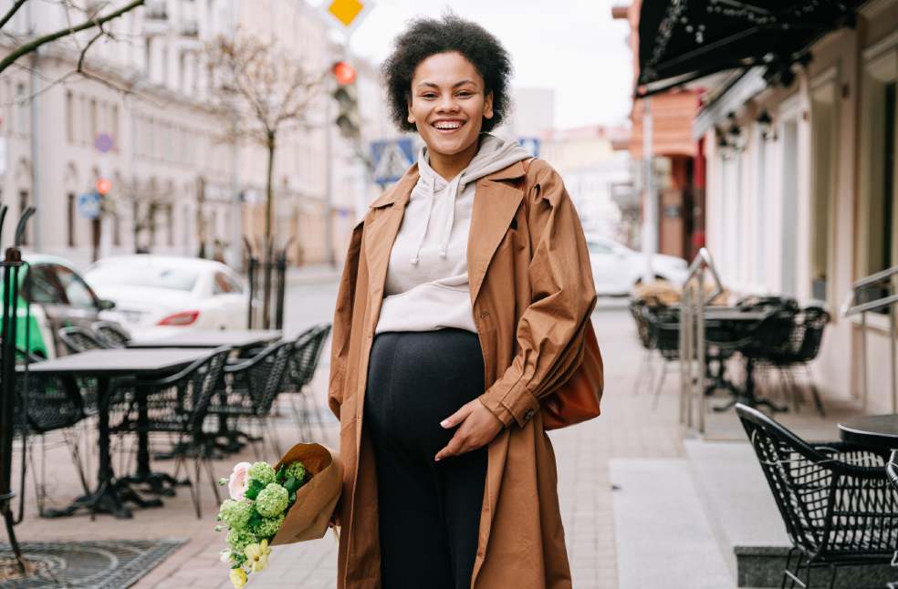 A joyful pregnant woman with a bouquet stands on a city sidewalk