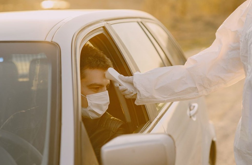 Healthcare worker in protective suit uses a thermal scanner to check temperature