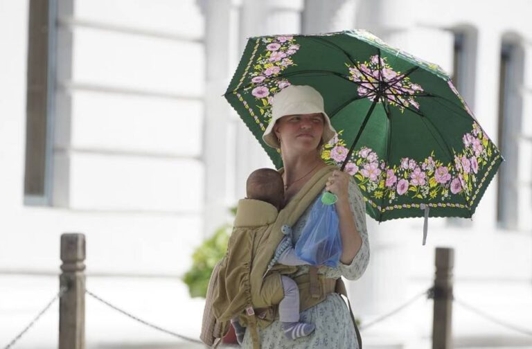 Spain battles extreme heatwave as temperatures climb Woman carrying baby in carrier with floral umbrella, enjoying a sunny day outdoors