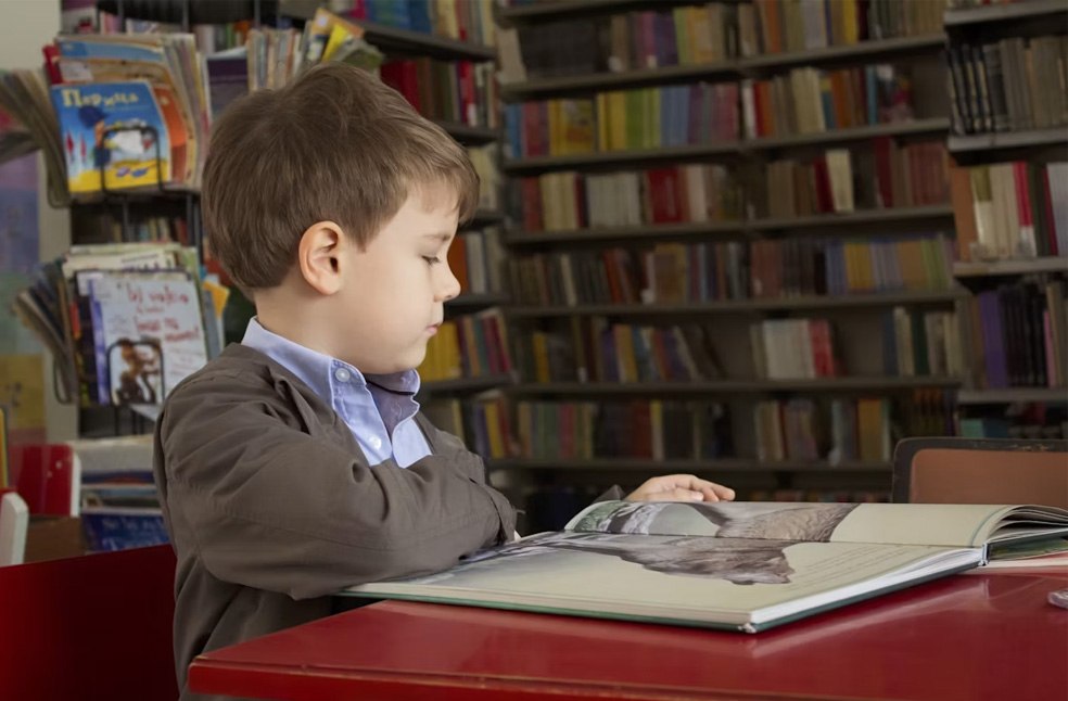 A boy sitting at a red table, reading a book