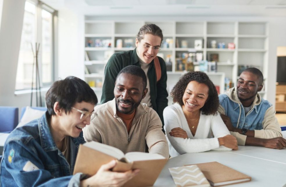 A group of diverse students smiling and studying together indoors in a library setting
