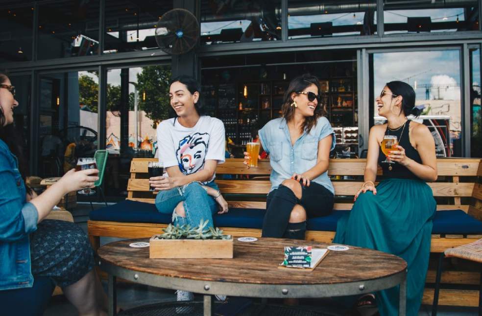 Four friends laughing and enjoying drinks together at an outdoor cafe setting