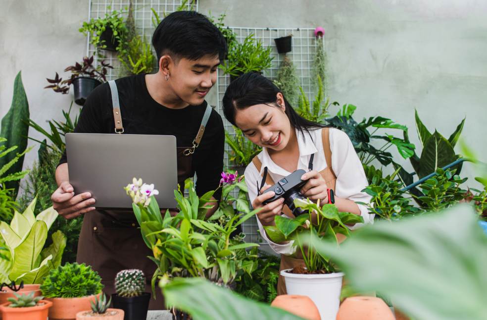 Young gardener couple wearing apron use laptop and camera
