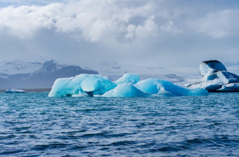 Arctic ice melt resumes with record winter reduction Majestic icebergs float on a serene glacier lagoon in Iceland, surrounded by snowy mountains under dramatic clouds