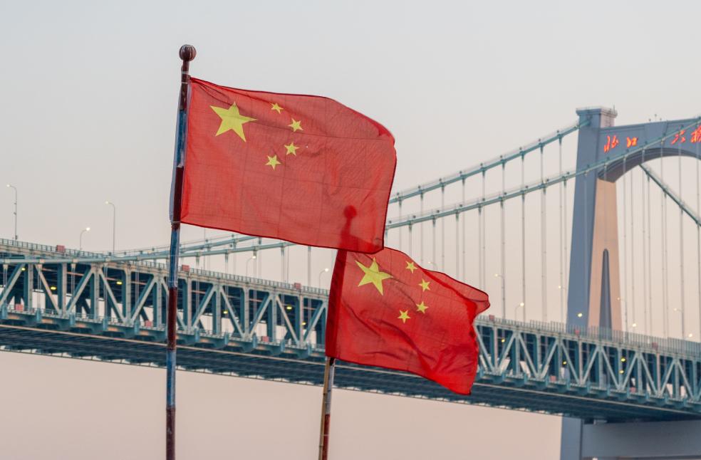 Chinese flags waving in front of a bridge at sunset