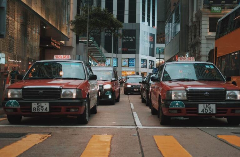 China cuts oil reliance through rapid EV taxi adoption Red taxis driving through a busy downtown street in Hong Kong, showcasing urban life and vibrant city atmosphere