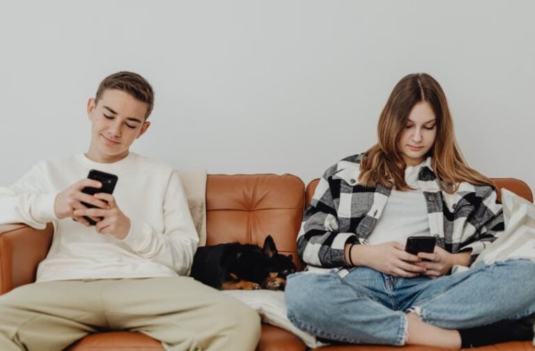 Study finds most Australian teens still on social media after ban Two teenagers sitting on a sofa with a dog, using social media