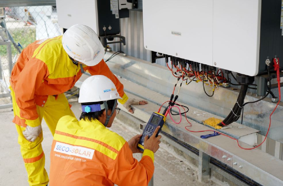 Two electrical engineers installing and testing solar power systems wearing safety gear at a construction site