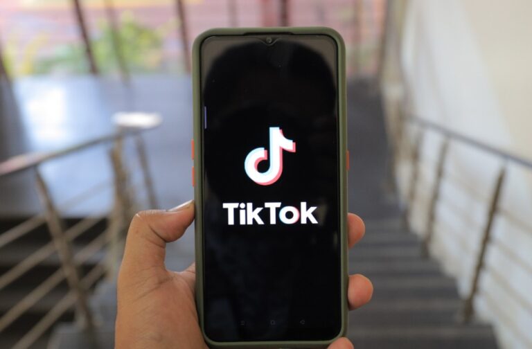UK regulator probes TikTok over child safety measures A close-up of a hand holding a smartphone displaying the TikTok app inside a modern building
