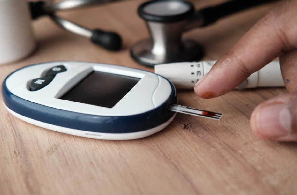 Close-up image of a glucometer checking blood sugar level with a finger pricking device nearby.