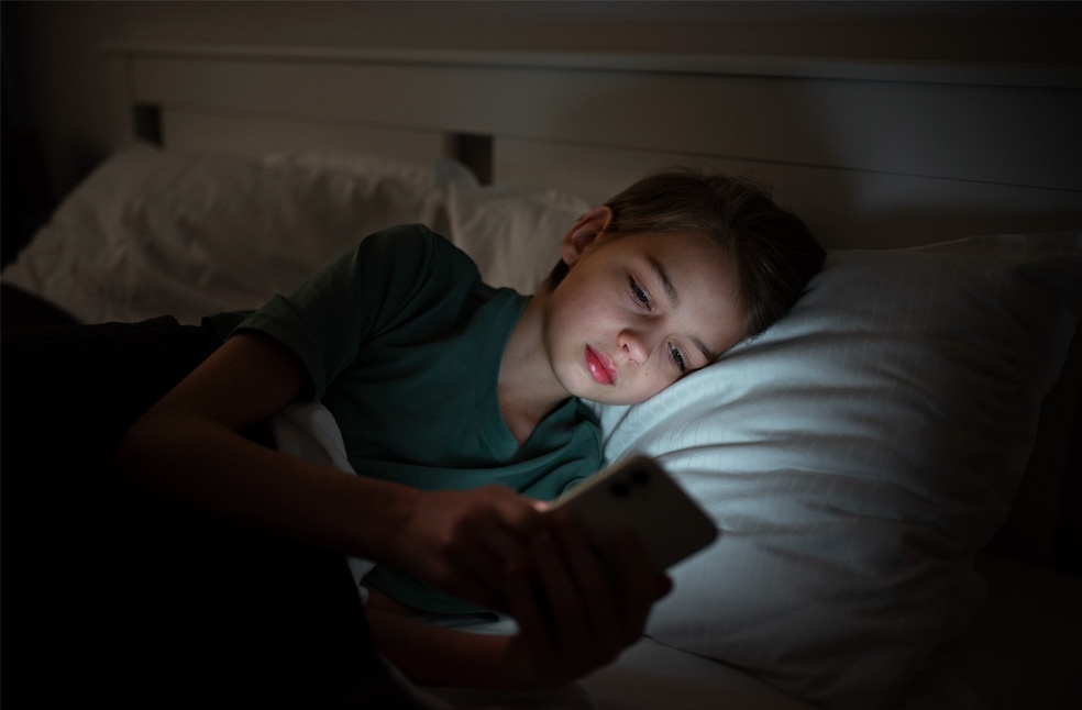 A teenage boy using a phone at night in bed