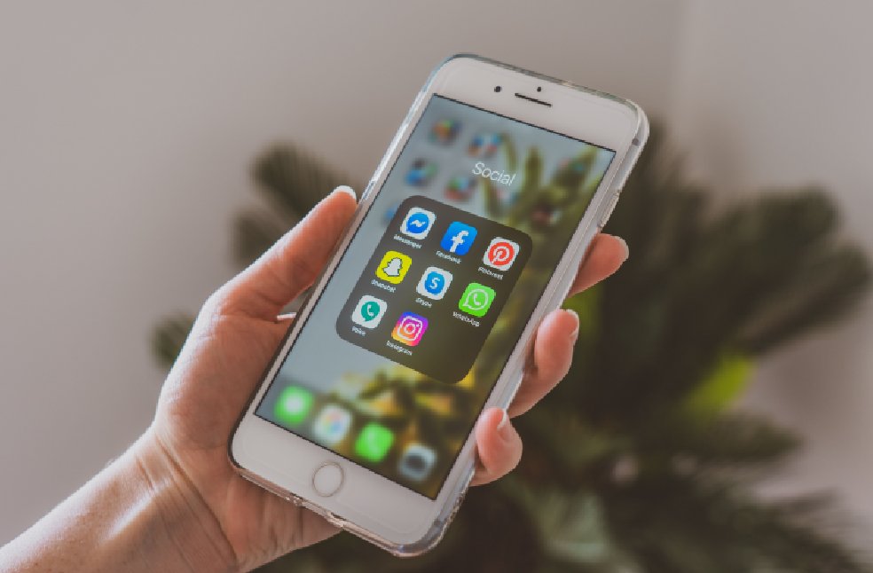 Close-up of a hand holding a smartphone displaying popular social media apps