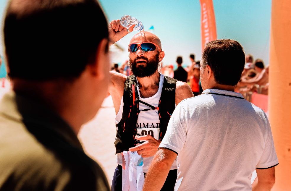 A male runner cools down with water during a summer marathon by the seaside.