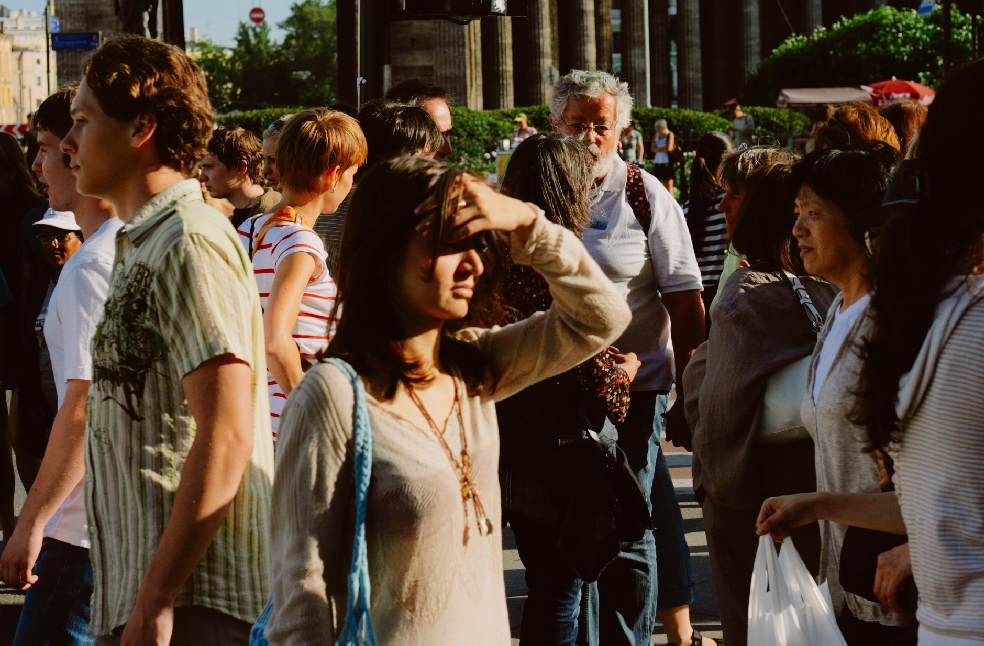 A bustling urban street scene with diverse people in summer attire enjoying a sunny day