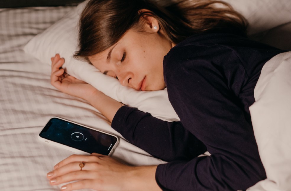 A woman peacefully sleeping in bed with a smartphone nearby, conveying rest and relaxation.