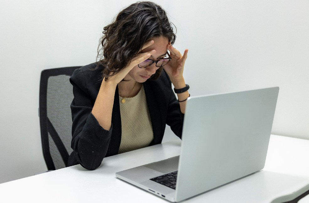 A young woman experiencing stress and fatigue while working on her laptop in an office setting.