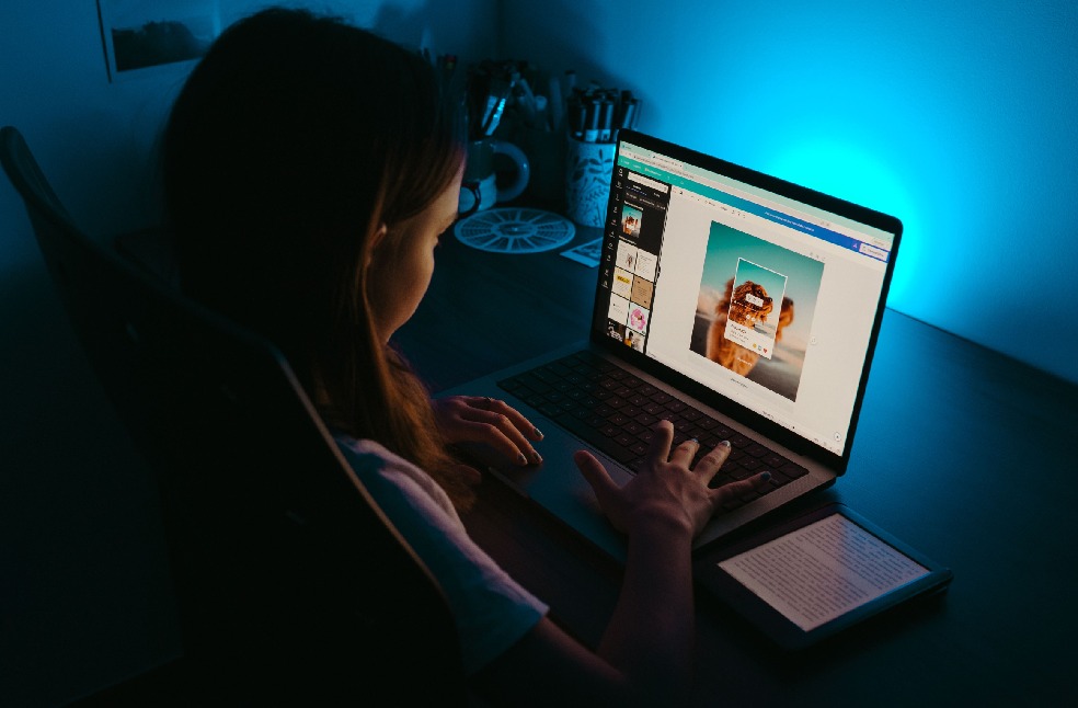 A girl uses a laptop at a desk in a dimly lit room, with a blue light creating a calm ambiance.