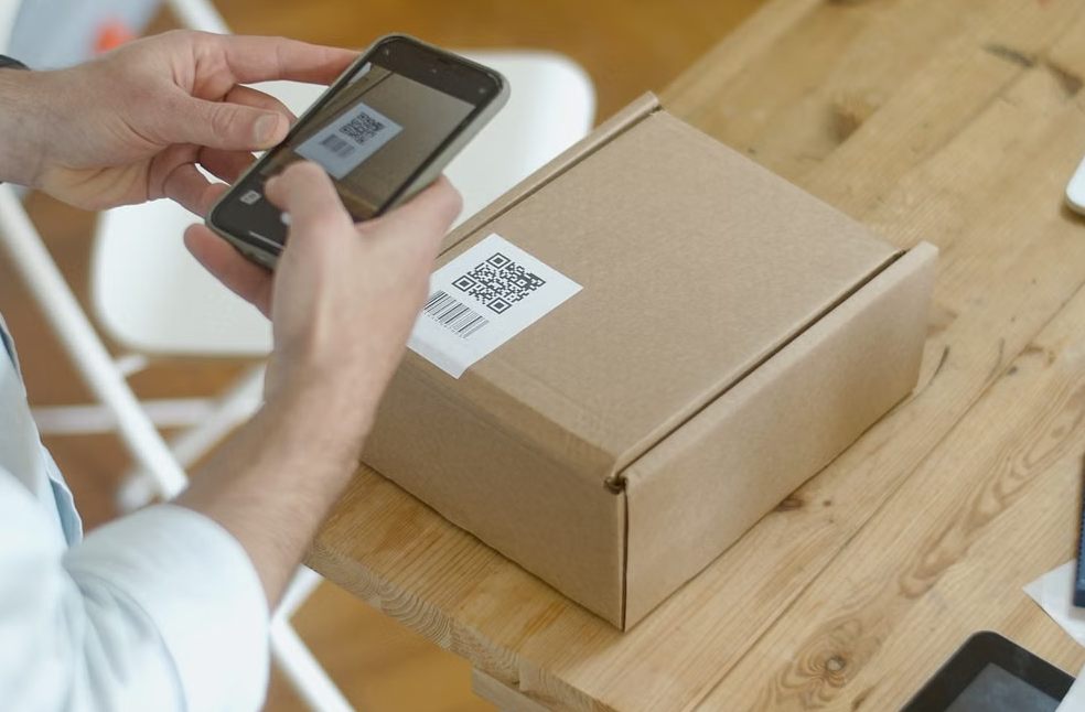 A person uses a smartphone to scan a QR code on a package in an online store setting