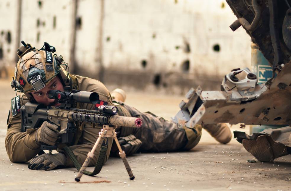 A soldier in tactical gear lying prone with a rifle in an urban setting