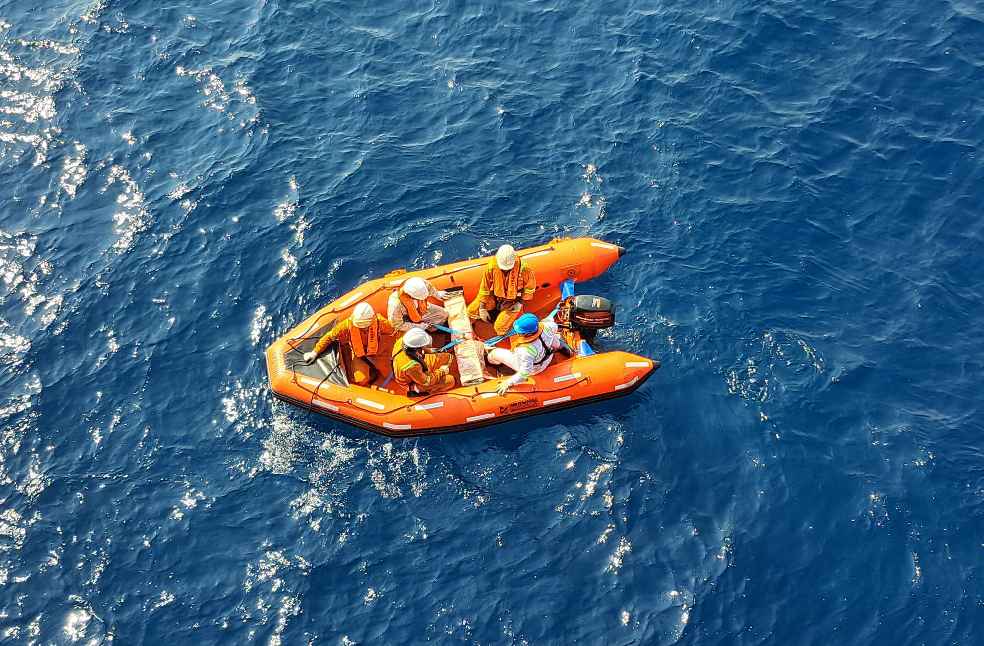 Safety crew on an orange inflatable rescue boat navigating the open sea.