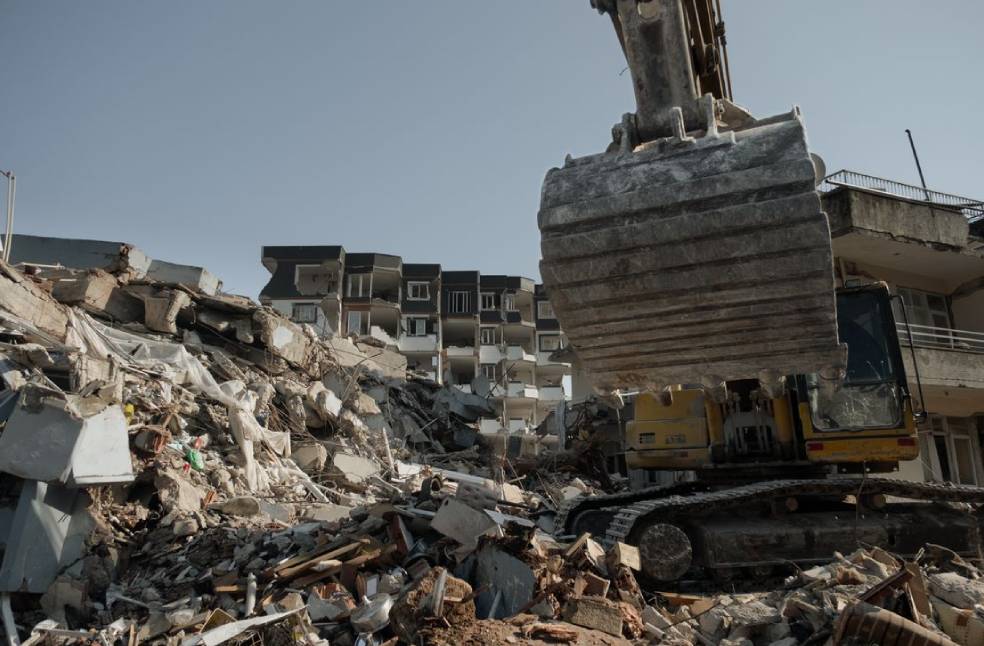 Powerful excavator clearing earthquake debris amidst building ruins