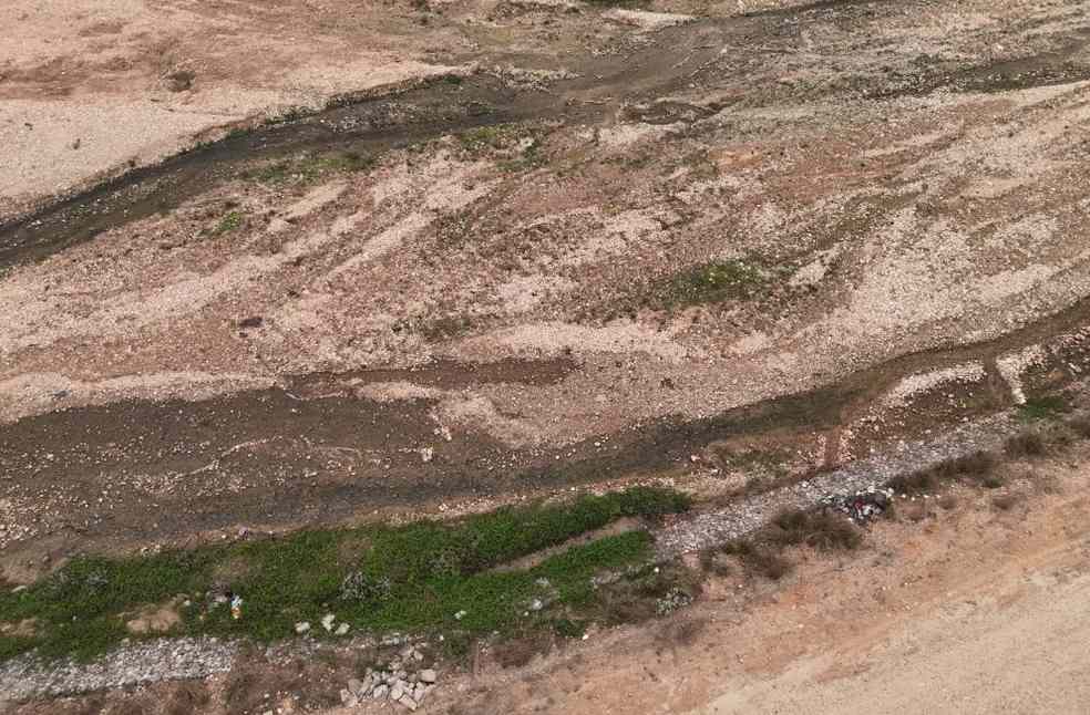 Aerial shot of a dry riverbed with rocky terrain, sparse vegetation, and exposed soil