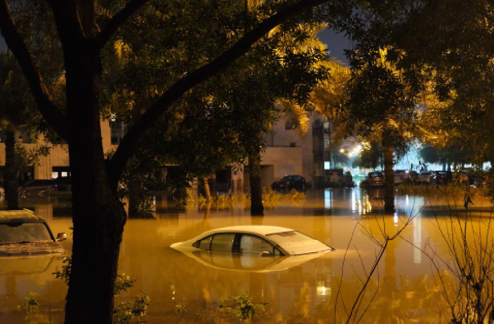 A dramatic scene of submerged cars in a flooded street surrounded by trees at night.