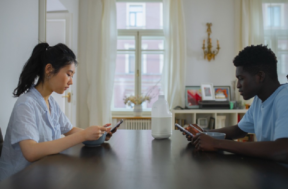 A couple engaging with their phones over breakfast, highlighting modern technology use in everyday life