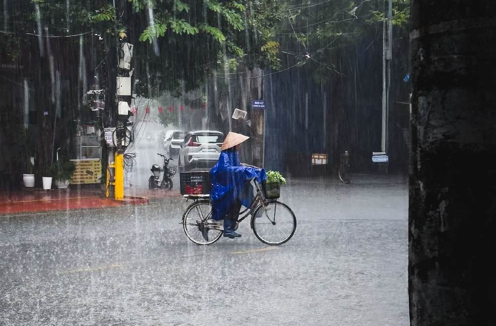 A person rides a bicycle through heavy rain in Haiphong, Vietnam, showcasing resilience and daily life.