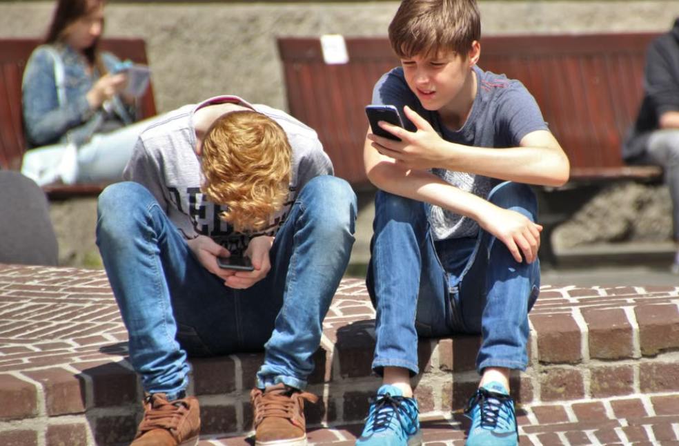 Two teenagers seated outdoors, focused on their smartphones