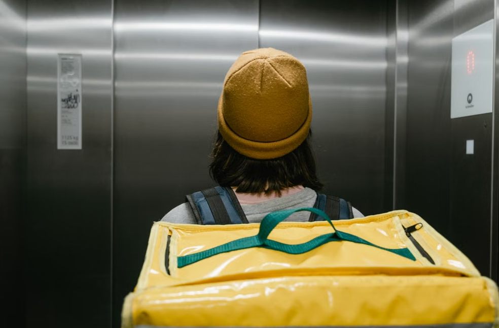 Back view of a delivery person with a yellow thermal bag inside an elevator
