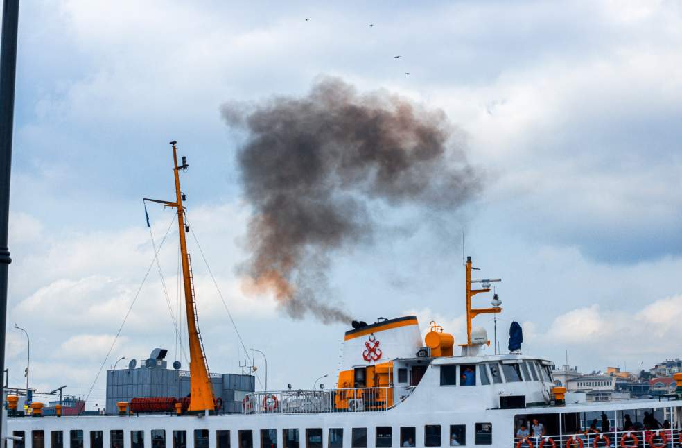 A passenger ferry emits dark smoke as it travels near the city harbor