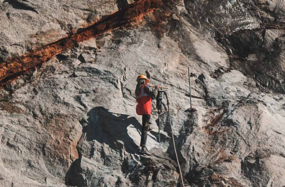 Construction worker drilling into rugged rock face, showcasing challenging outdoor work.