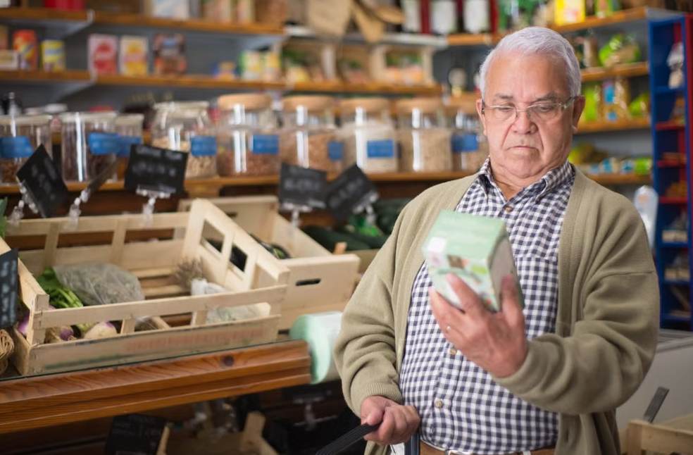 Elderly man examines product in grocery store aisle