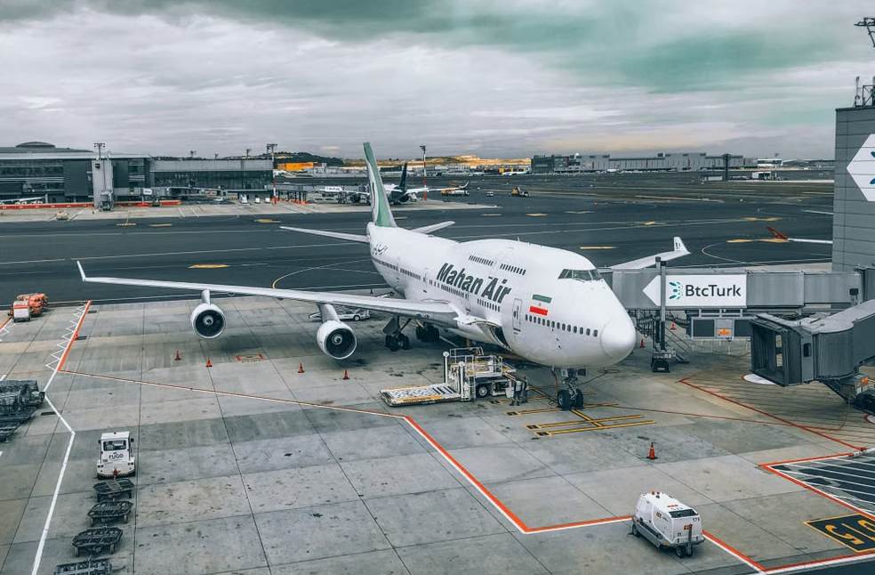 A Mahan Air Boeing 747 aircraft parked at a bustling airport terminal under cloudy skies