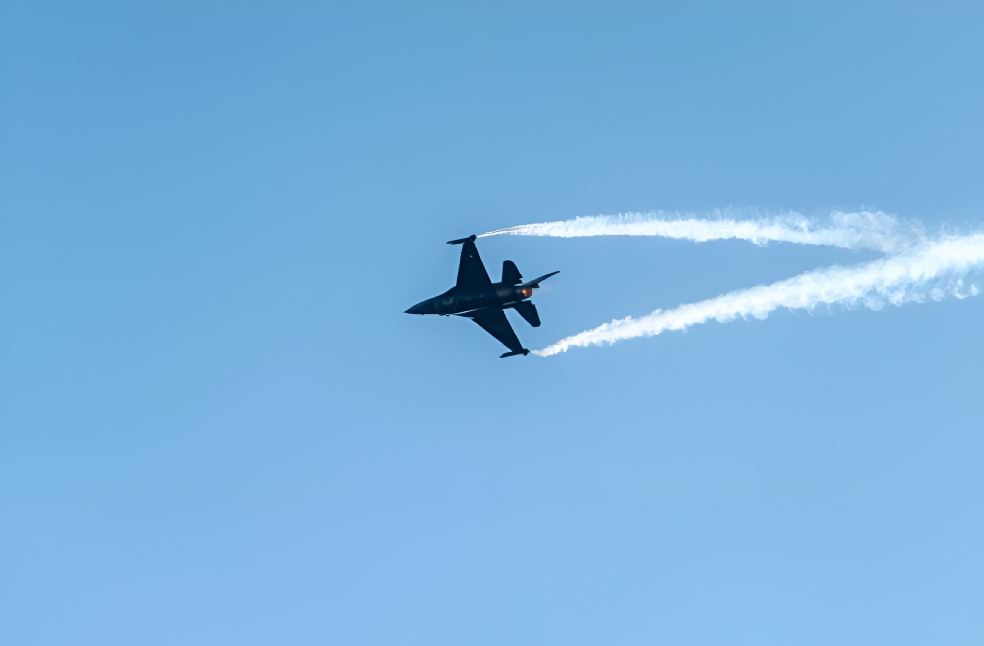 Jet fighter flying with contrails in a bright blue sky.