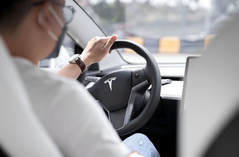 Tesla faces trial over racial discrimination against workers Close-up photo of a person driving a Tesla, showcasing modern vehicle interior design.